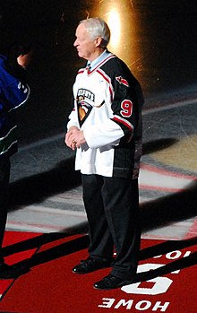 Photo couleur de Gordon Howe de profil sur un tapis rouge où son inscrits son nom et le numéro 9.