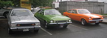 Trois voitures, une grise, une verte et une orange, sur un parking.