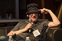 Piskor seated, wearing headphones and speaking into a microphone