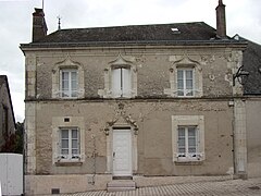 Photographie en couleurs d'une maison à étage dont le tympan de la porte d'entrée et le linteau des fenêtres est ouvragé.