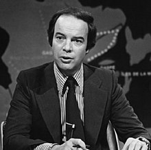 Black and white photo of Nadeau in a suit and tie behind a desk on a television news set