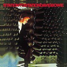 A colour photo of a man stepping into a room filled with cylindrical bars with "STATIONTOSTATIONDAVIDBOWIE" in red text at the top