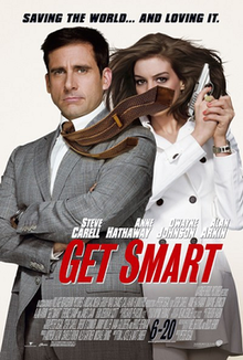 Maxwell Smart wearing suit and holding a gun, his tie blown to the side, covering the face of Agent 99 who is standing behind him wearing a white jacket.