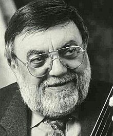 Publicity shot of smiling man with spectacles, short but full white beard, and greying hair.