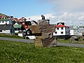 Skúvoy village, seen from nearby the church. In the foreground is a sculpture made by Hans Pauli Olsen, it depicts Sigmundur Brestisson as a child and a boat.