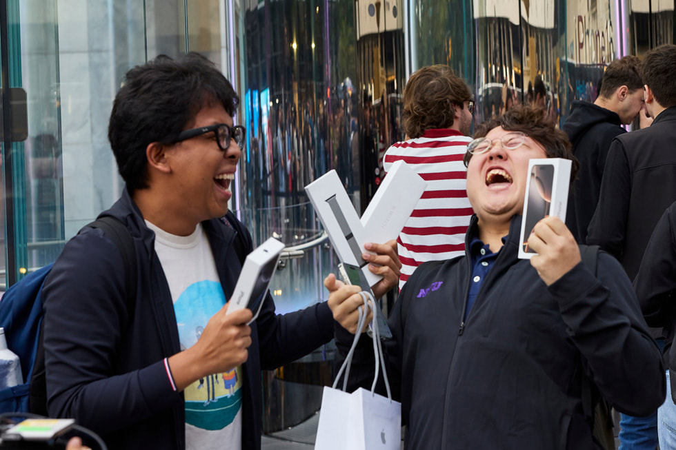 Two laughing customers hold up their new purchases at Apple Fifth Avenue in New York City.