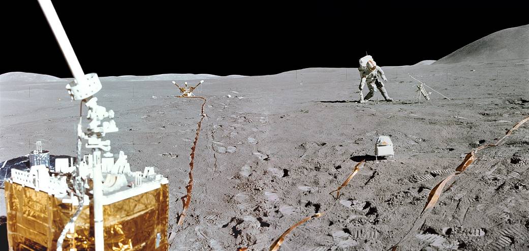 Panorama of lunar surface with instruments in foreground and astronaut in spacesuit in far right