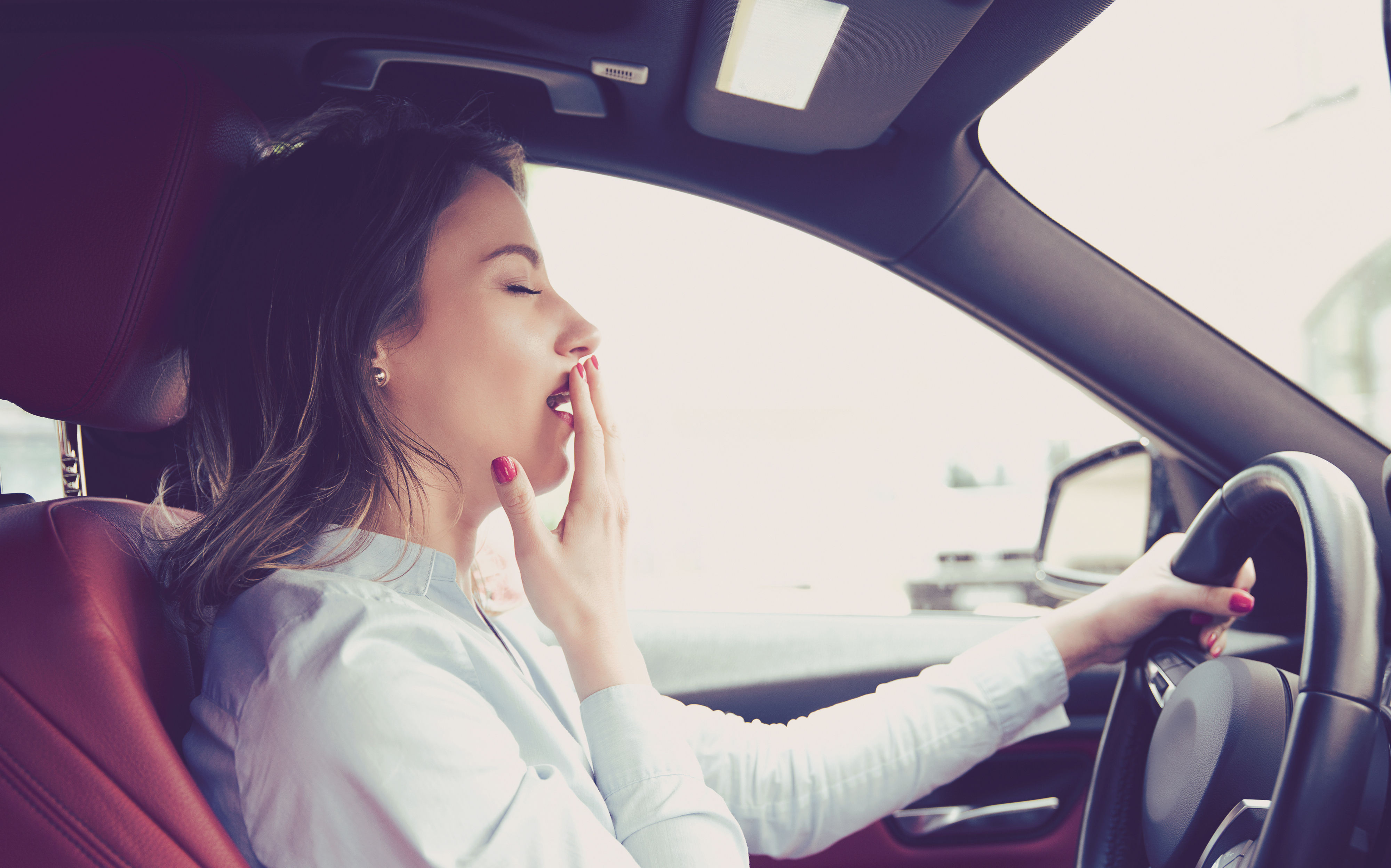 a woman yawning in the driver 's seat of a car