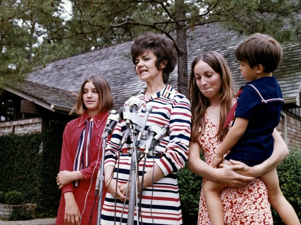 A woman in '70s attire with her three children in front of a microphone