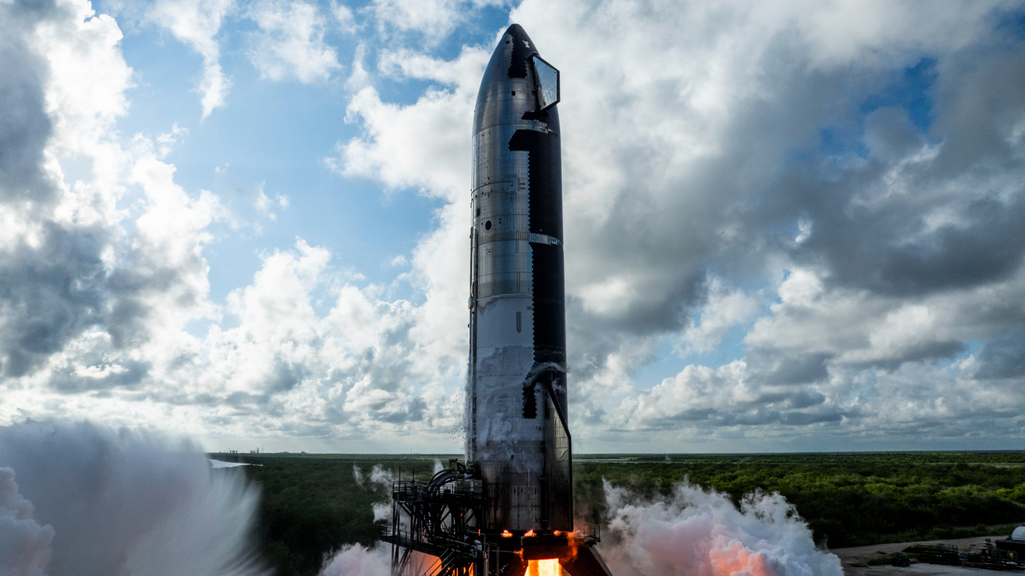 a silver rocket conducts an engine test with a cloudy sky in the background