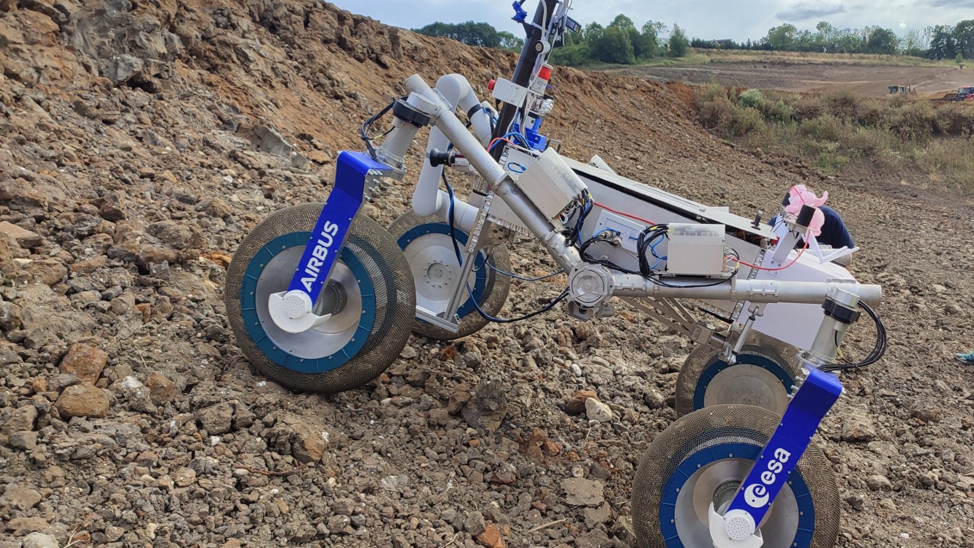 a four-wheeled rover drives in red dirt on a construction site