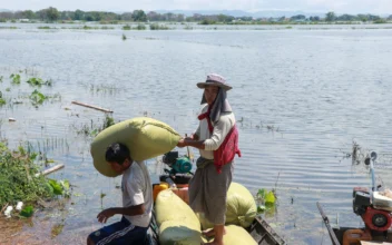 Farmers carry bags of rice next to flood waters as they evacuate their homes near Phayarphyu village in Loikaw township in Burma's Karenni state on Sept. 16, 2024. (STR/AFP via Getty Images)