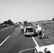 Mord an Brigitte Wetzenstein-Ollenschläger: Bundesautobahn A 1 bei Reinfeld: Leichenfundort im Graben neben Seitenstreifen am 19. August 1972: abgesperrter Fahrbahnstreifen mit Polizeifahrzeugen am Straßenrand: dazwischen Polizeibeamte: hinten Mitte wegfahrender Trecker nach Mähen eines Teils des Grases und des angrenzenden Getreidefeldes: hinten links mehrere fahrende Pkws: hinten Bäume