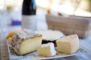 various wedges of cheese spread out on a plate with a bottle of wine in the background